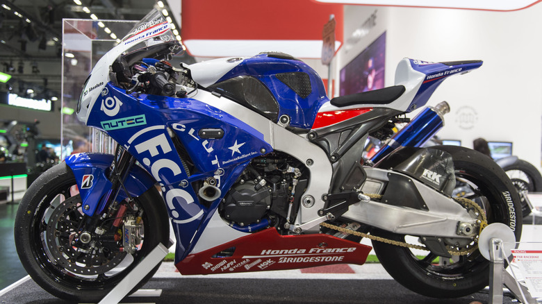A blue and white Honda CBR1000RR on a stand indoors in a large warehouse at a trade fair in 2018.