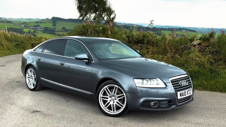 Front 3/4 view of a gray C6 Audi A6 Le Mans, UK plates, countryside in the background