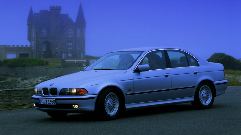 Front 3/4 view of an E39 BMW 5 Series, castle in the background, intensely blue dusk sky