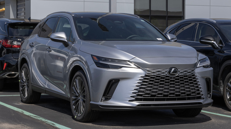 A silver Genesis GV80 parked on a car park next to other SUVs.