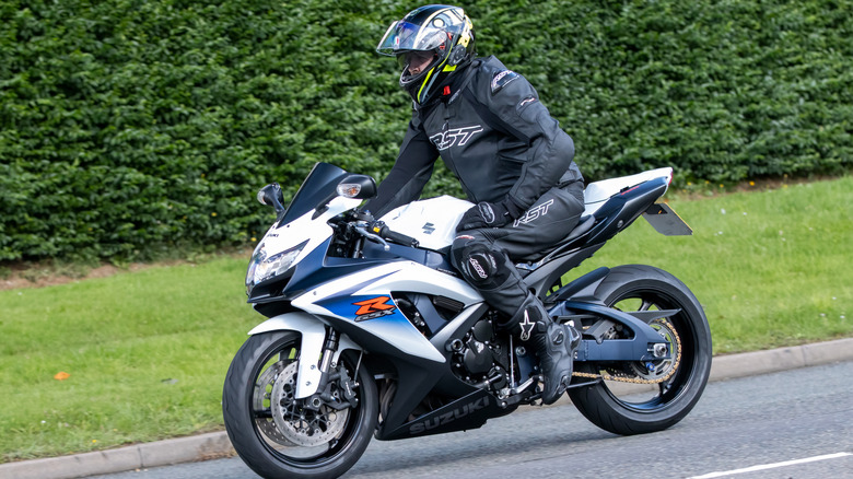 Suzuki GSX-R750 with rider in parking lot in front of green shrubs