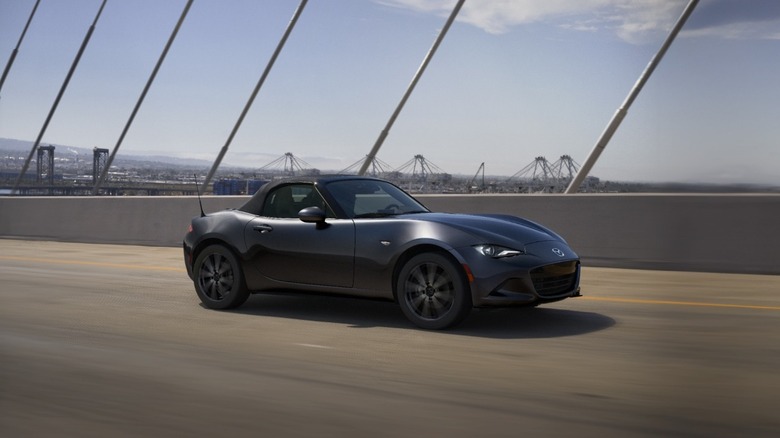 The new Mazda Miata in gray driving on a bridge, front 3/4 view, roof closed
