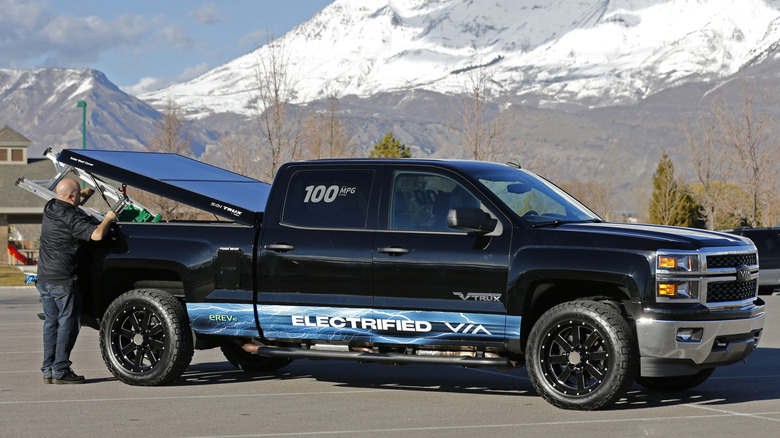 VIew of man lifting solar tonneau cover on black Chevy Silverado pickup truck.
