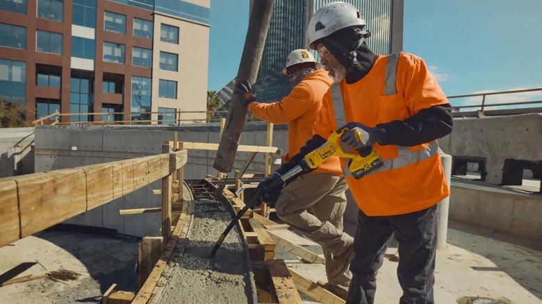 A person using a DeWalt concrete vibrator on a job site.