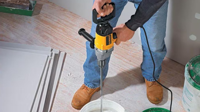A person using a DeWalt mixer on concrete.