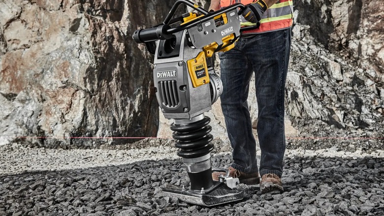 A person using a DeWalt rammer on stone.