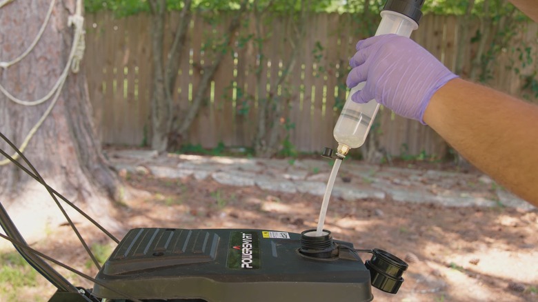 A person siphoning gas from a lawn mower.