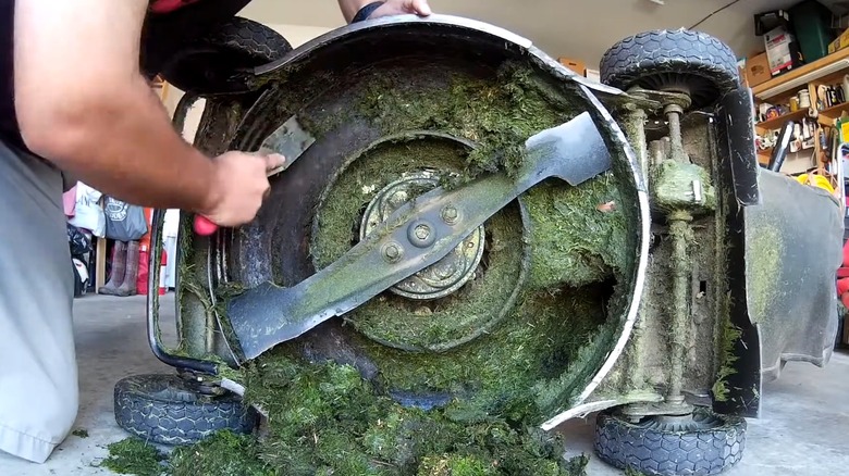 A person using a lawn mower scraper on a mower deck.