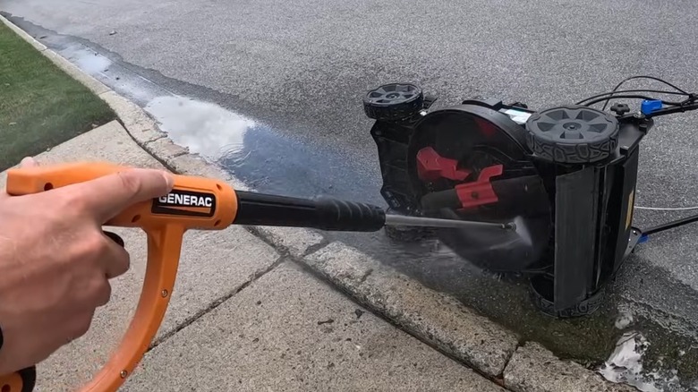 A person pressure washing a lawn mower deck.