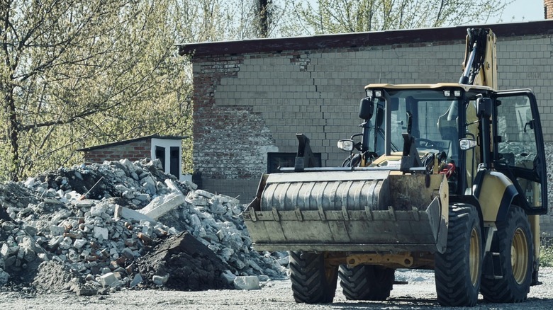 Yellow backhoe loader standing near a pile of rubble