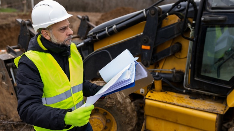 Site engineer inspects backhoe loader