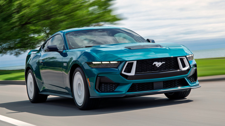 Front 3/4 view of green 2026 Ford Mustang GT driving on coastal road.