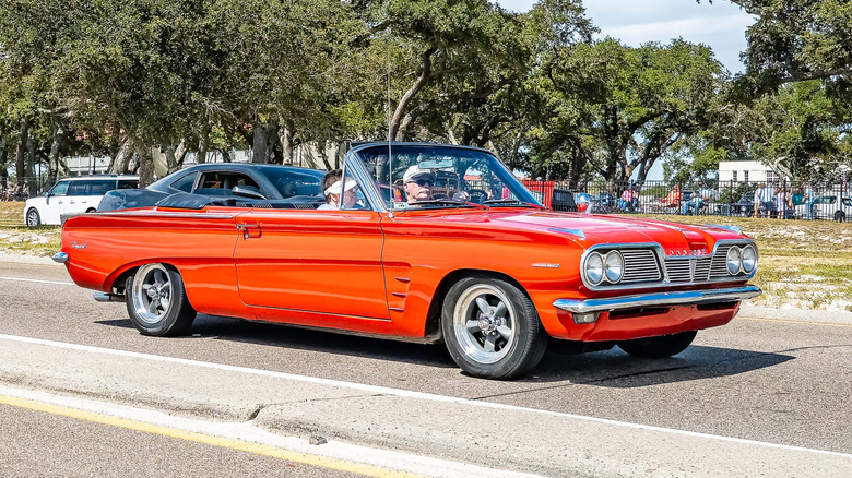 Front 3/4 view of orange 1962 Pontiac Tempest cruising near car show.