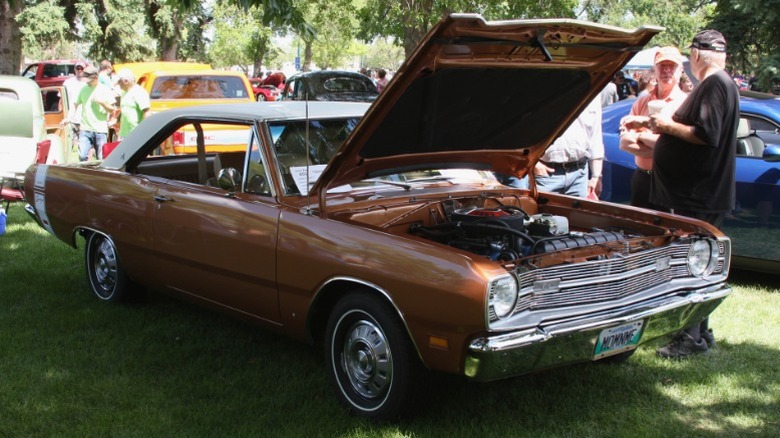 Brown 1969 Dodge Dart parked on grass at a car show with hood open.