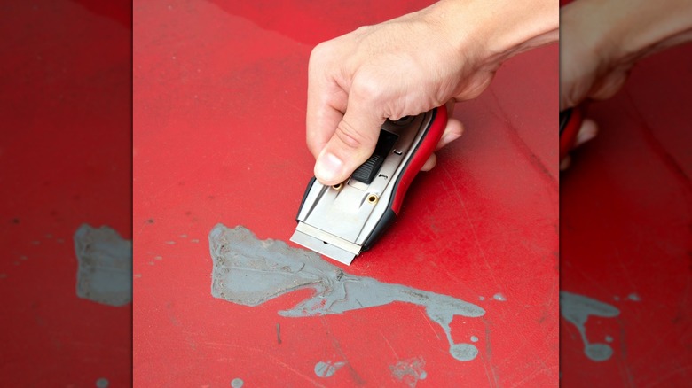 close up of a hand scraping grey paint from a red floor
