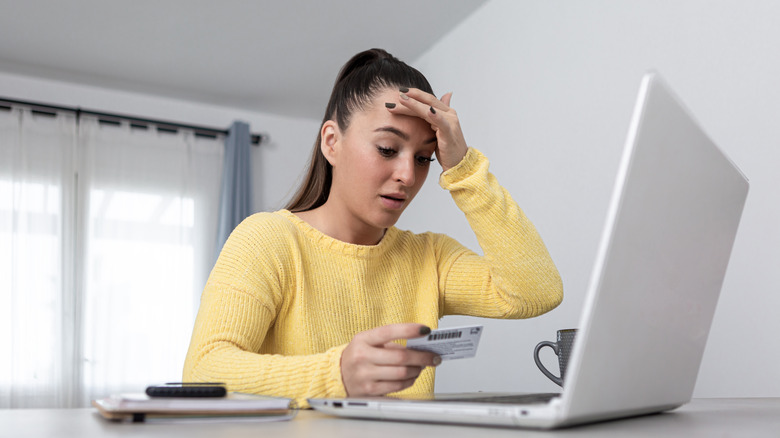 Stressed out woman holding a card in her hand and looking at computer