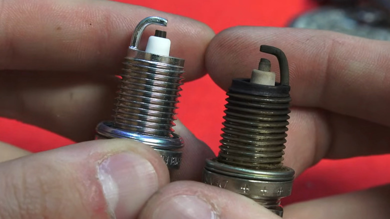 Person comparing two spark plugs by holding them next to each other