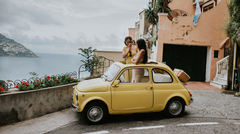 Two girls standing inside a small car, passing through the sunroof