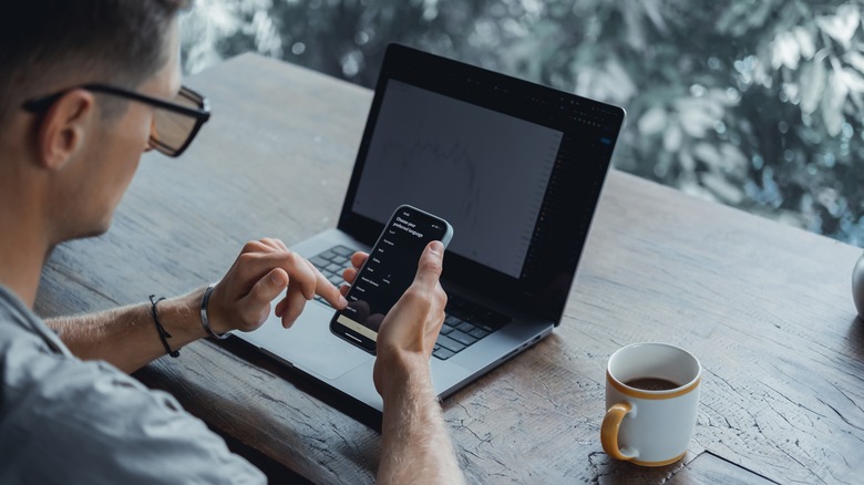 Man at his computer, holding an iPhone