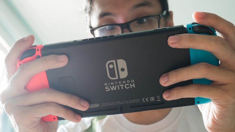guy with black-rimmed glasses holding a Nintendo Switch