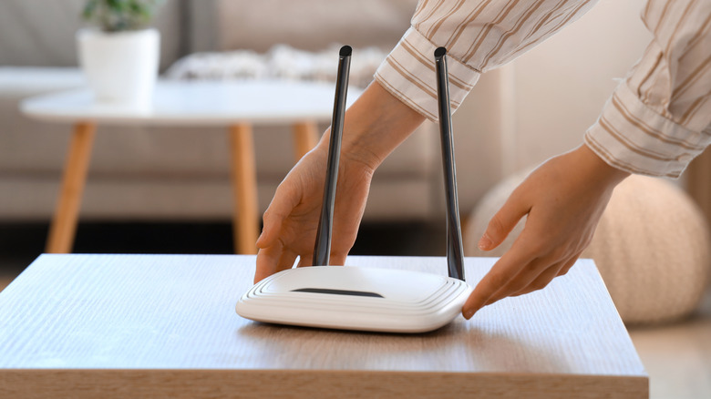 A person placing a Wi-Fi router on top of a table.