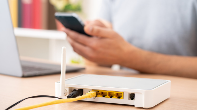 A person using a phone and a laptop next to a router