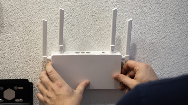 A person installing a Wi-Fi router with four antenne on a white wall