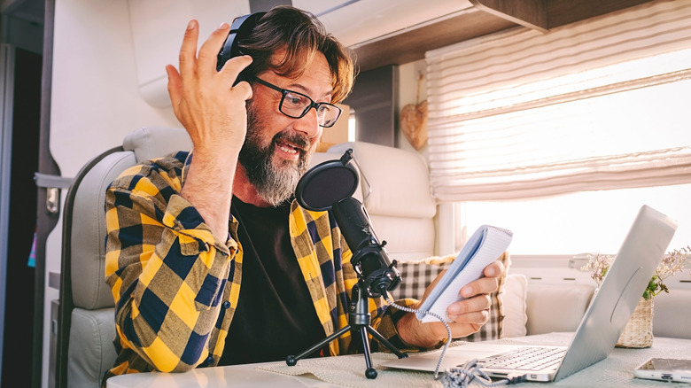 Man in camper with laptop, headphones, and microphone recording a podcast