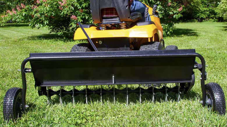 A riding mower pulling an aerator and spreader combo attachment