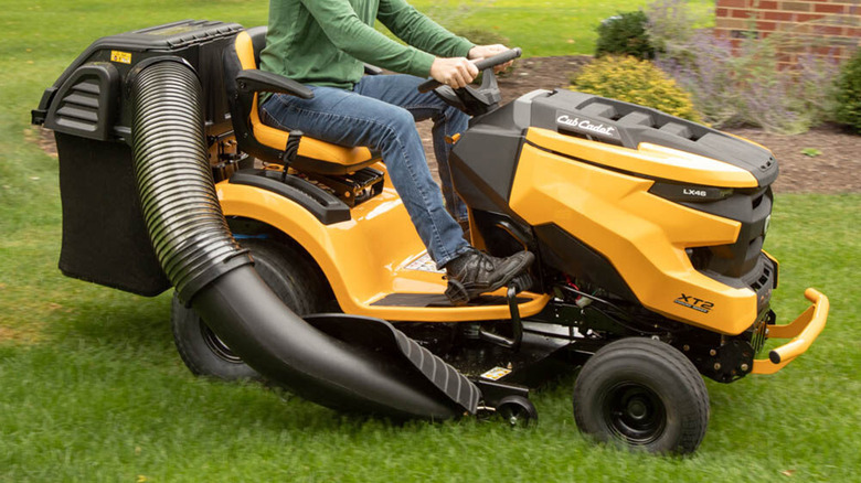 A person mowing grass with a bagger on their riding mower