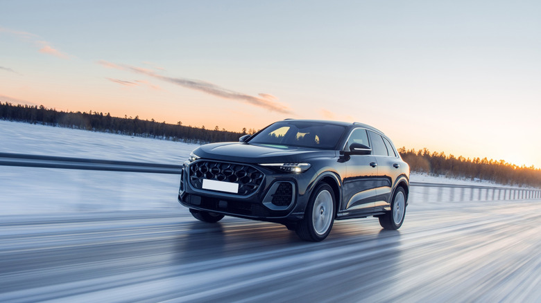A sleek black modern SUV driving at high speed on a snow-covered highway during a vibrant sunset.