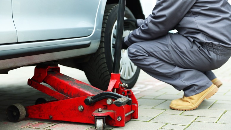 A worker using a floor jack on a vehicle to check a tire's wheel bearings.