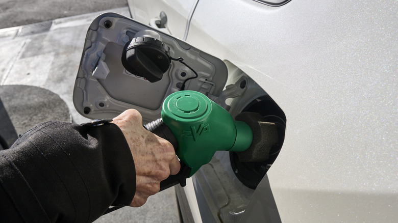 Driver filling silver car with gas with green-handled pump