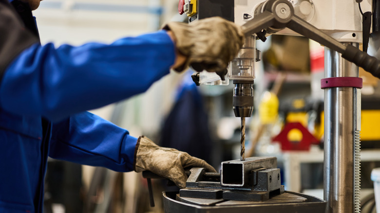 A person out of shot using a drill press to cut metal stock