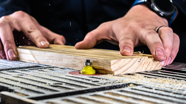 Closeup of two hands using a piece of wood on a router table