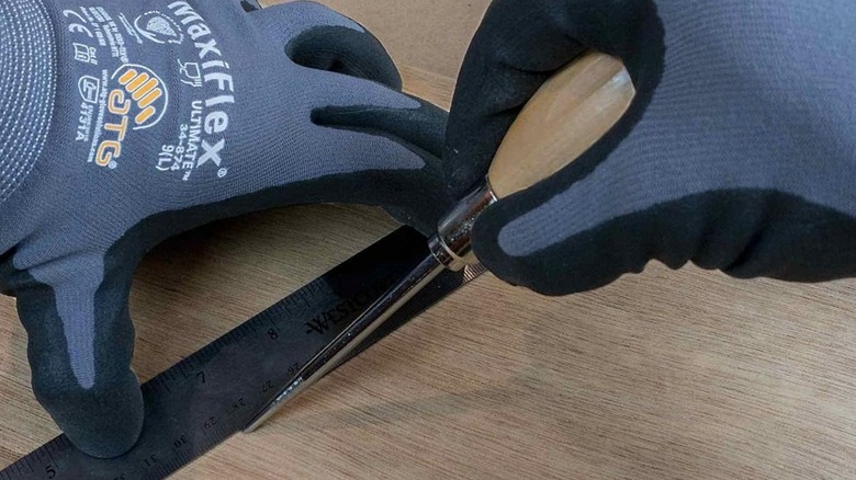 A person marking a board with a General Tools Scratch Awl.