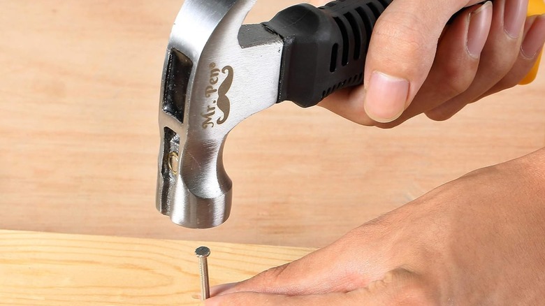 A person pounding a nail on a board with a Mr. Pen Claw Hammer.