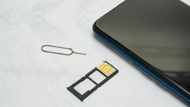 An Android phone with a dual SIM tray resting on a table with a SIM extractor tool