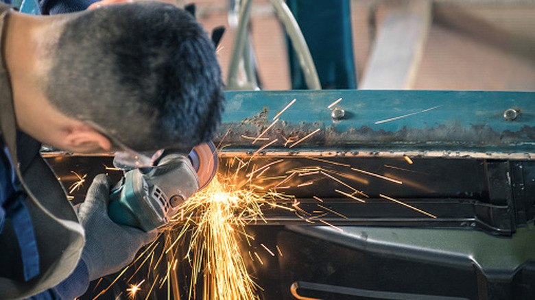 Mechanic grinding classic car bodywork with grinder wheel
