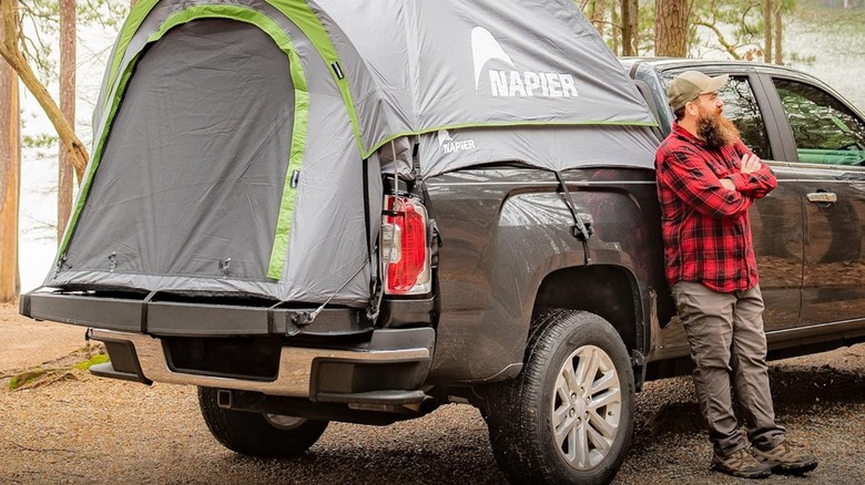 A tent by Napier mounted on the bed of a pickup truck, a man stands nearby