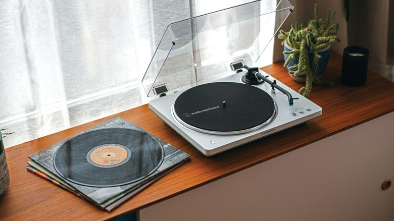 White Audio-Technica AT-LP70XBT on a table next to a stack of vinyl record.