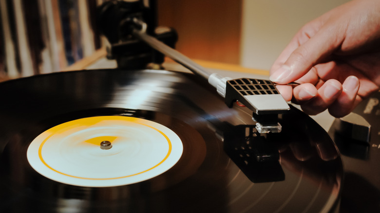 Close-up of a hand dropping a cartridge onto a vinyl record.