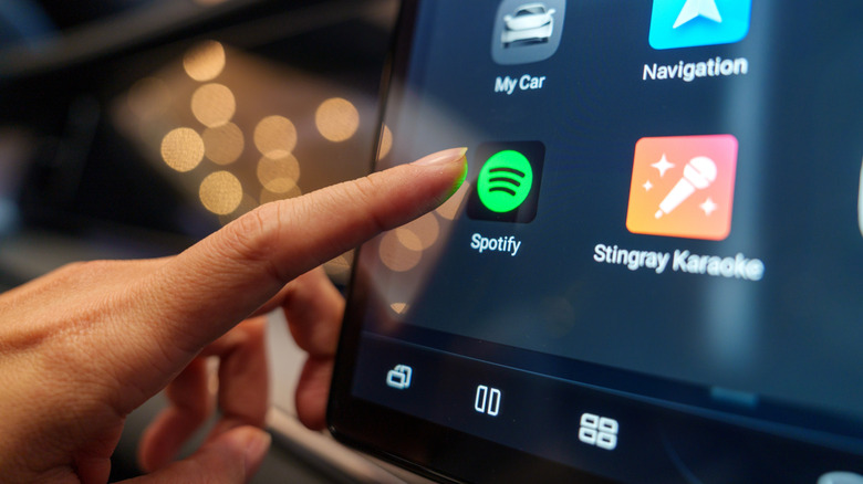 A close up of a finger is about to press the Spotify icon on a car screen