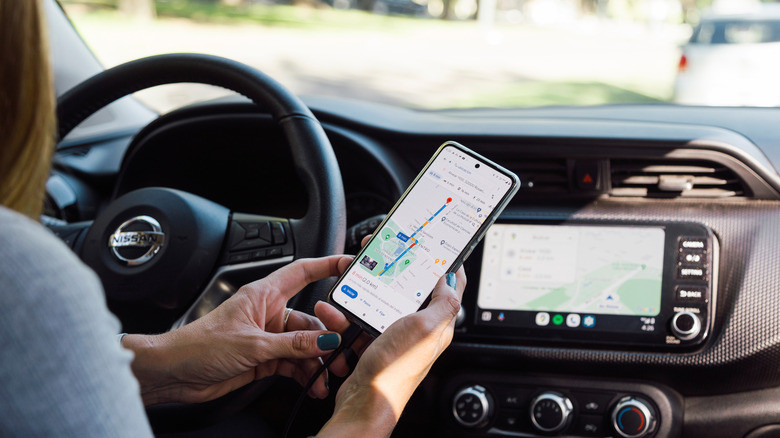 A female driver is comparing Google Maps on her phone with the Google Maps on her car screen