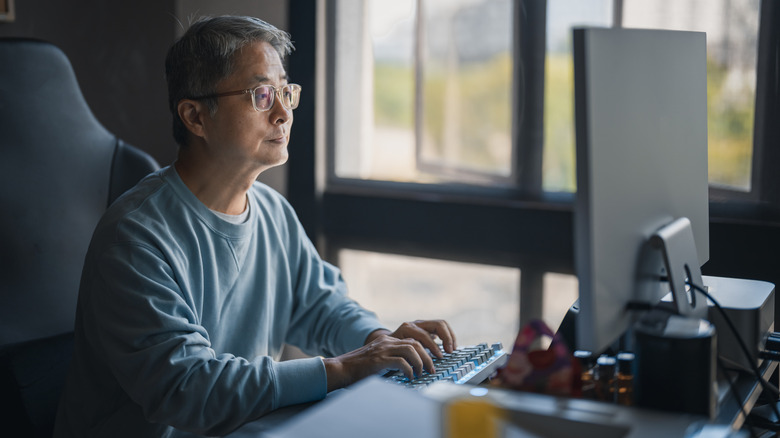 A man sitting at a home work desk with a view out the window