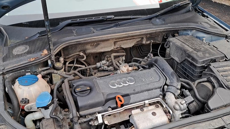 A blue 2012 Audi A3 with its hood open, displaying a muddy 1.4 liter engine cover with the TFSI badging on it.