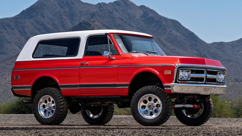 Front 3/4 view of red, restomodded GMC Jimmy parked in front of desert mountains.