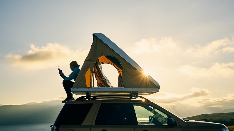 Person sitting on top of vehcile roof with rooftent open
