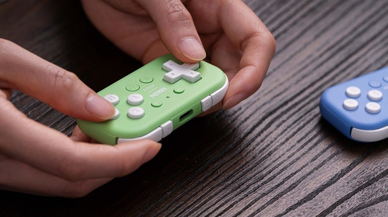 A person holding the 8BitDo Micro controller with another nearby.