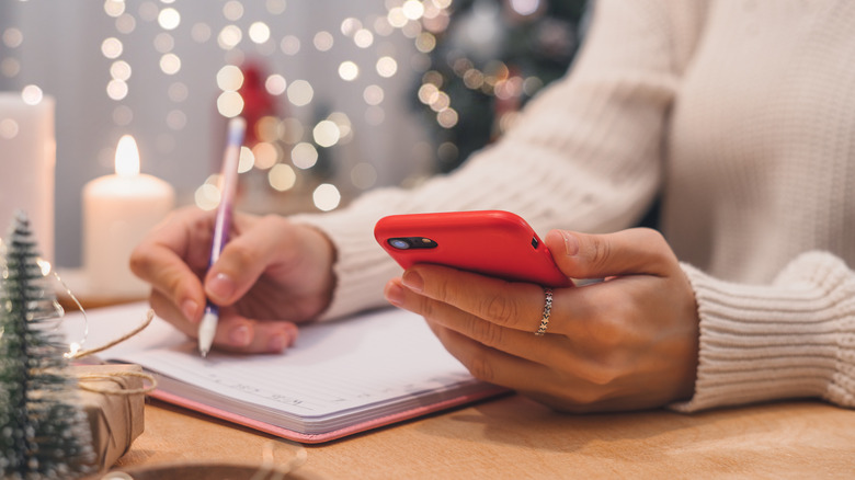 Person on phone and taking notes surrounded by holiday lights.